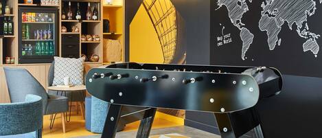 A pool table in a room with a 'SHOP' sign, a world map mural, and a cozy seating area.