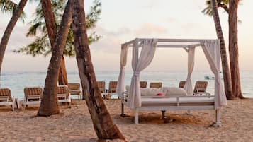 Un paisaje playero con una cama con dosel, sillas de playa y palmeras.