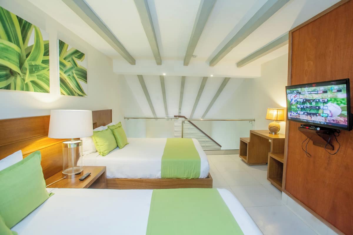 A hotel room with a bed, a TV, a lamp, a nightstand, a wooden desk, and a staircase.