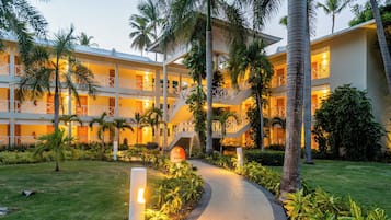 A multi-story hotel with a central courtyard, palm trees, and a pathway leading to the entrance.