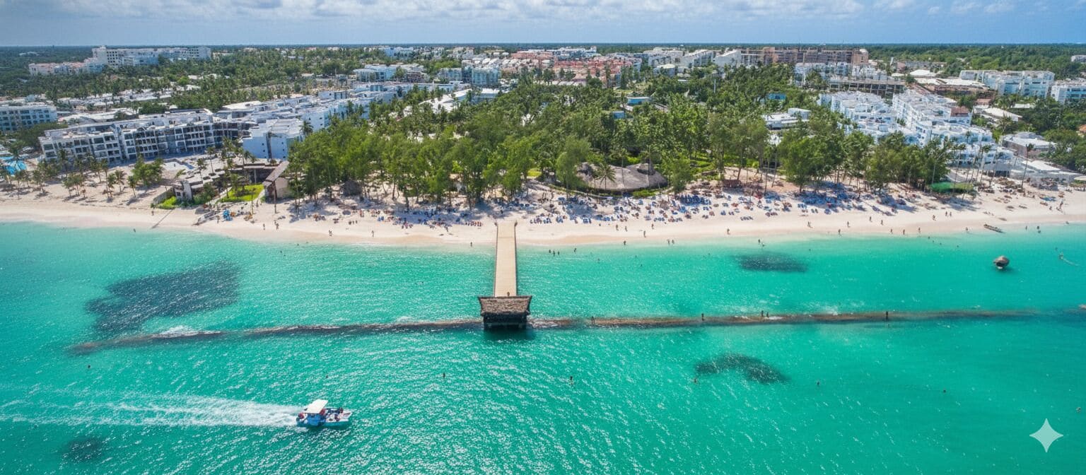 An aerial view of a coastal resort with a sandy beach, a pier extending into the turquoise waters, and a backdrop of resort buildings.