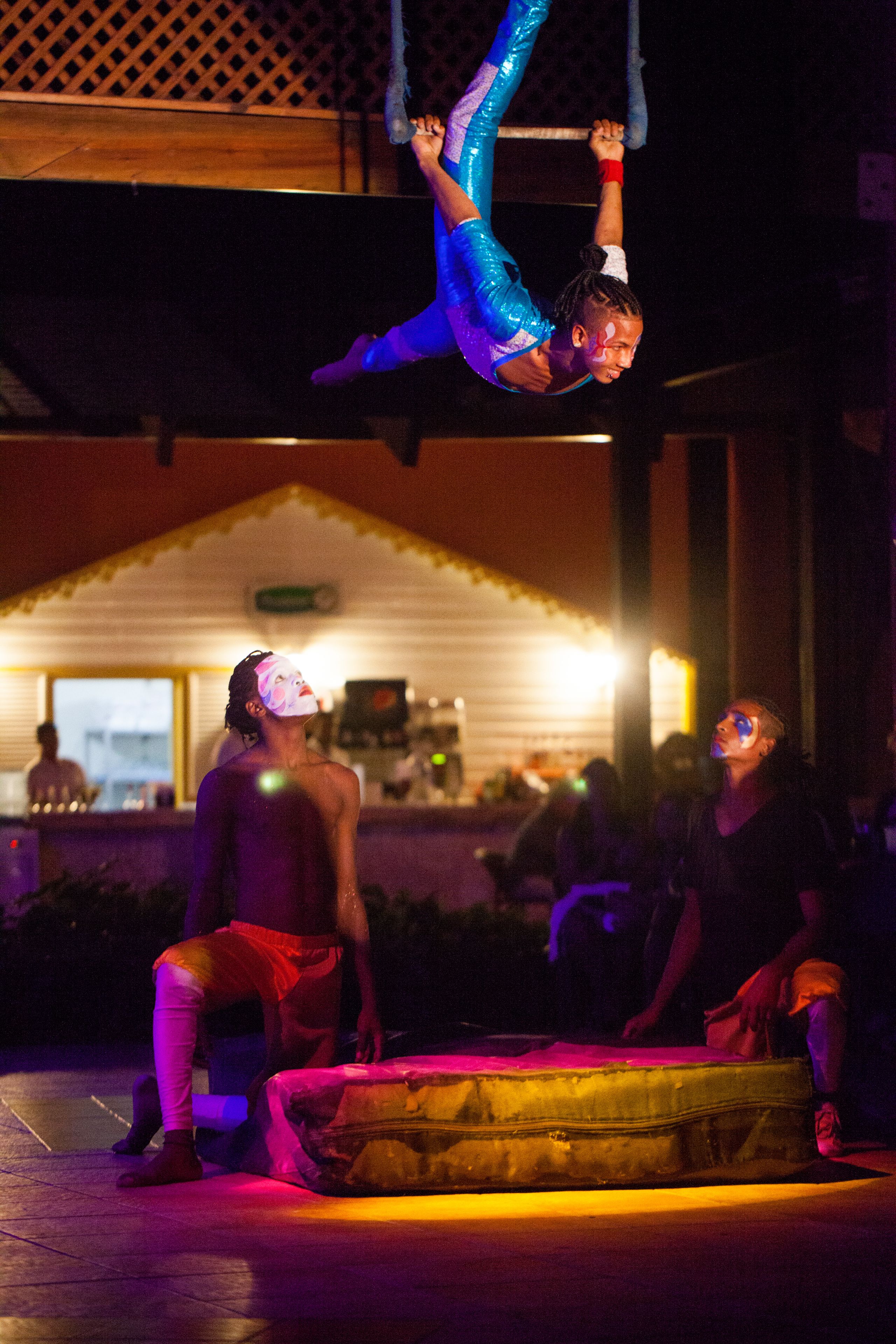 Una persona realizando una acrobacia aérea en un entorno exterior con poca luz y un edificio al fondo.