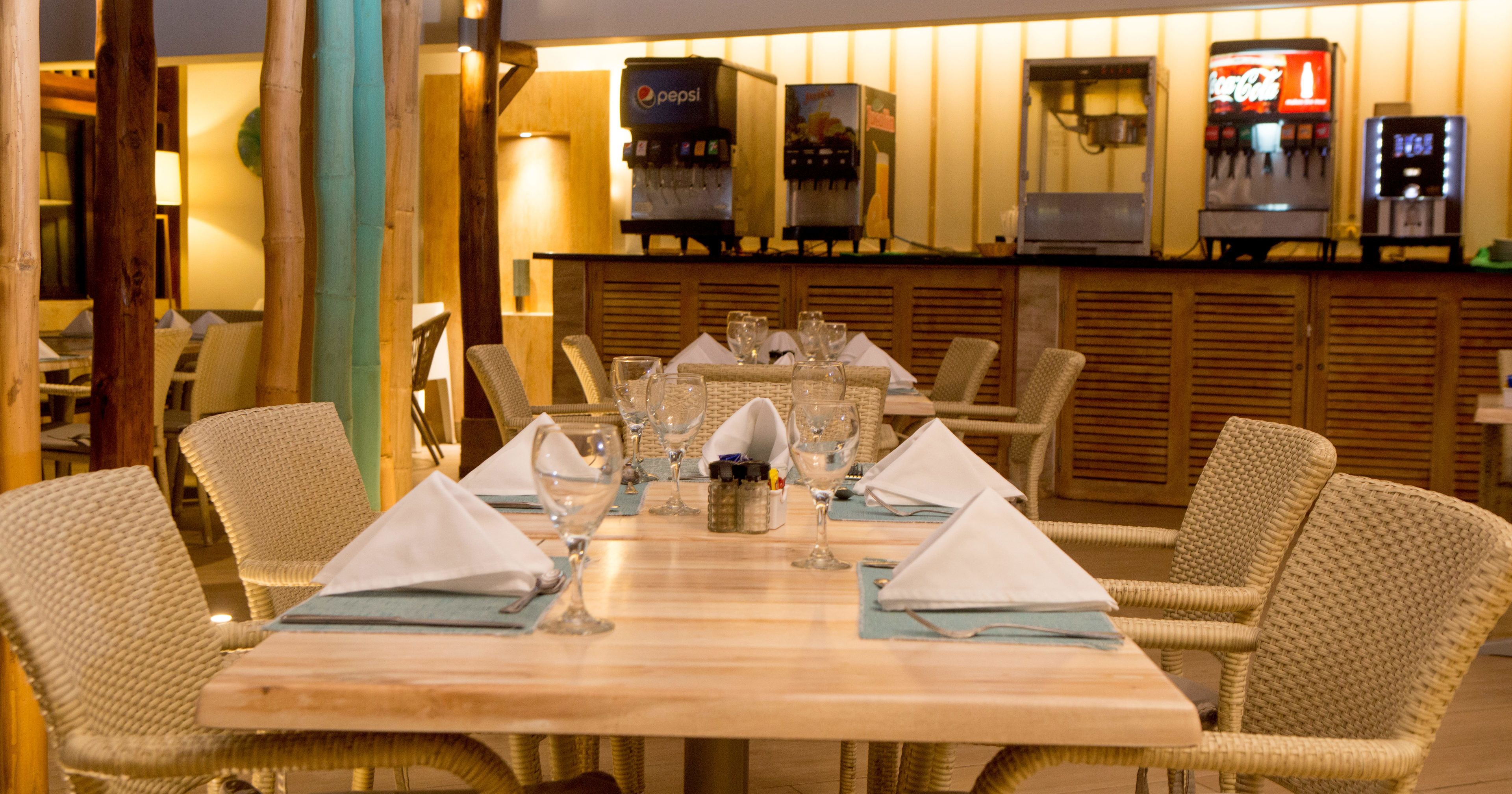 Un restaurante con una larga mesa de madera dispuesta para comer, rodeada de sillas de mimbre.