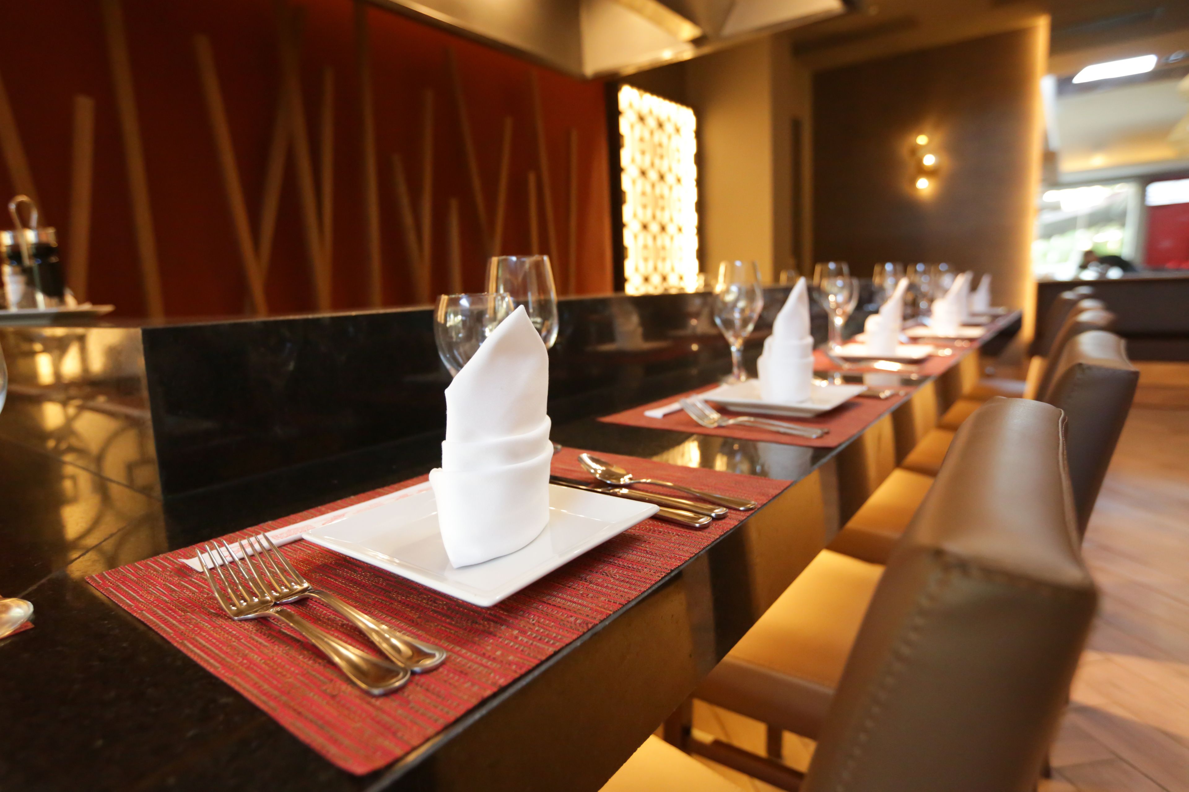 Une rangée de tables dressées dans un restaurant, avec une disposition soignée comprenant des assiettes, des couverts et des serviettes.