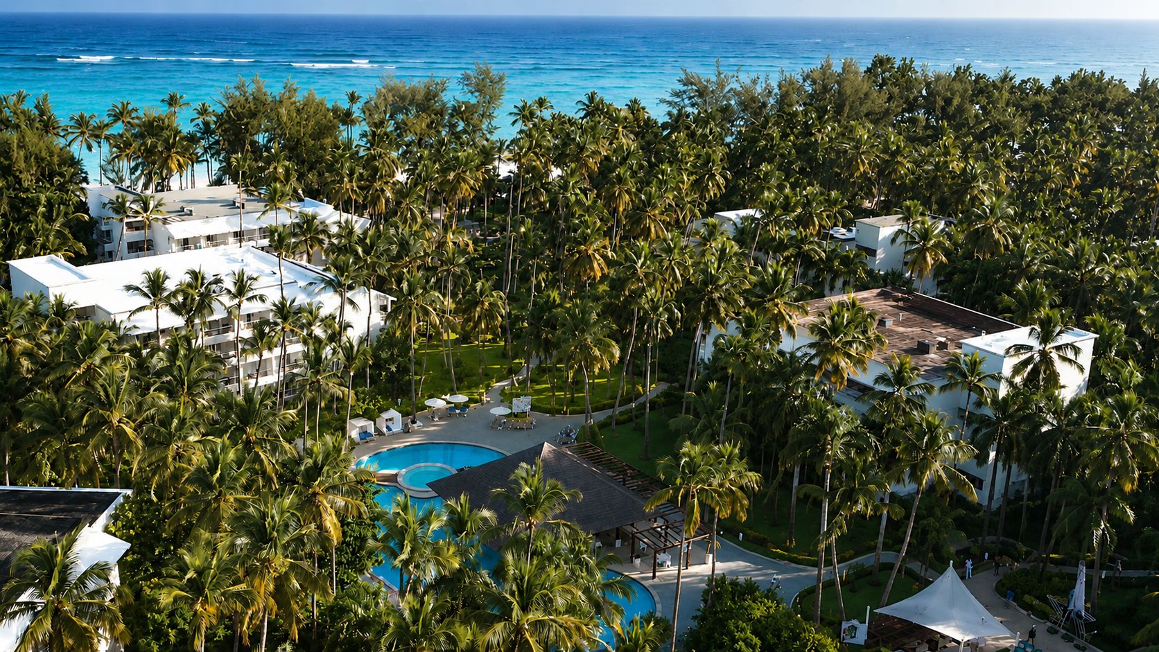 A resort with a swimming pool surrounded by palm trees and a view of the ocean.
