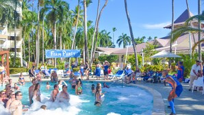 Ein Poolbereich mit badenden Personen, umgeben von Palmen und Liegestühlen.