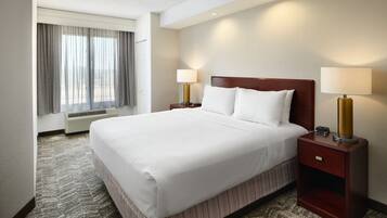 A hotel room with a large bed, two bedside tables with lamps, a window with curtains, and a carpeted floor.
