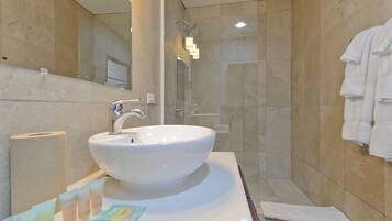 Un baño con un lavamanos grande de color blanco, un espejo y una cabina de ducha de vidrio.
