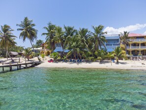 Un resort en la playa con agua turquesa cristalina, palmeras y un edificio con techo azul.