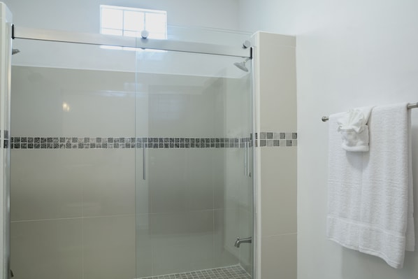 Um chuveiro com paredes de vidro, chão de azulejos e uma toalha branca pendurada em um suporte de metal.