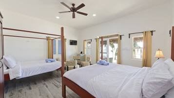 Une chambre d’hôtel avec deux lits simples, un ventilateur de plafond, un bureau avec une chaise et un téléviseur fixé au mur.