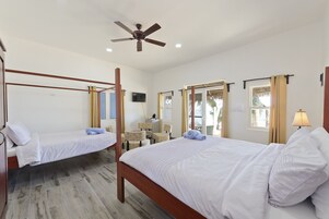 Una habitación de hotel con dos camas individuales, un ventilador de techo, un escritorio con una silla y un televisor en la pared.