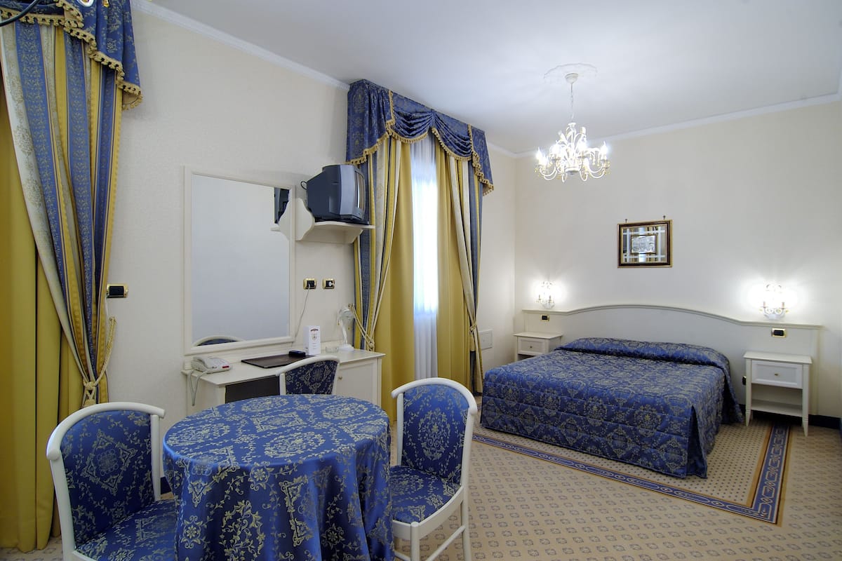 Ein Hotelzimmer mit Bett, Schreibtisch, Sessel, Tisch, Fernseher und einer Chandelier.