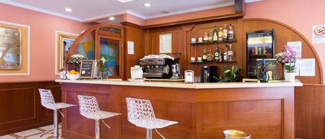 A bar area with a wooden counter, bar stools, and a coffee machine.