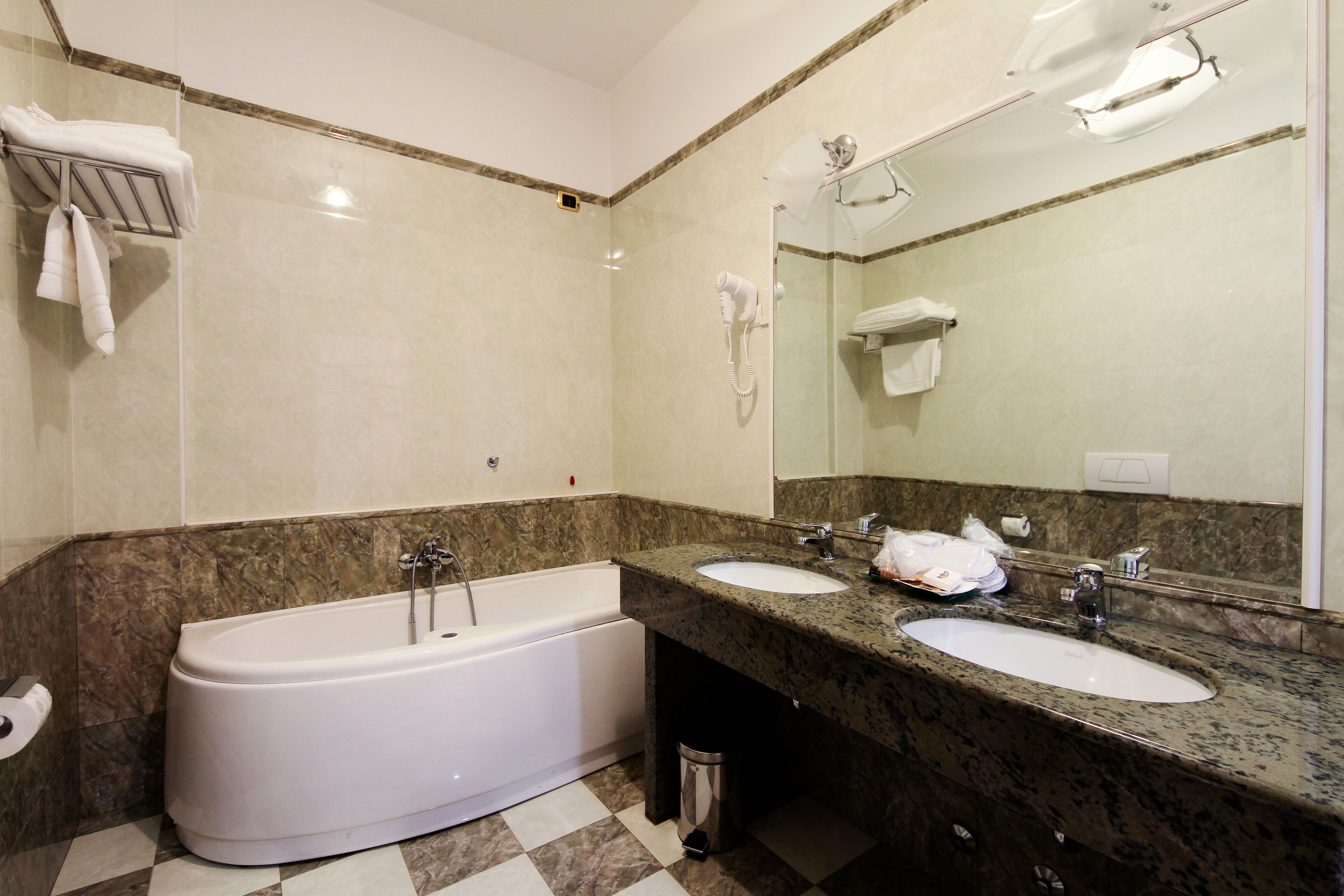 A bathroom with a bathtub, two sinks, a large mirror, and a trash can.