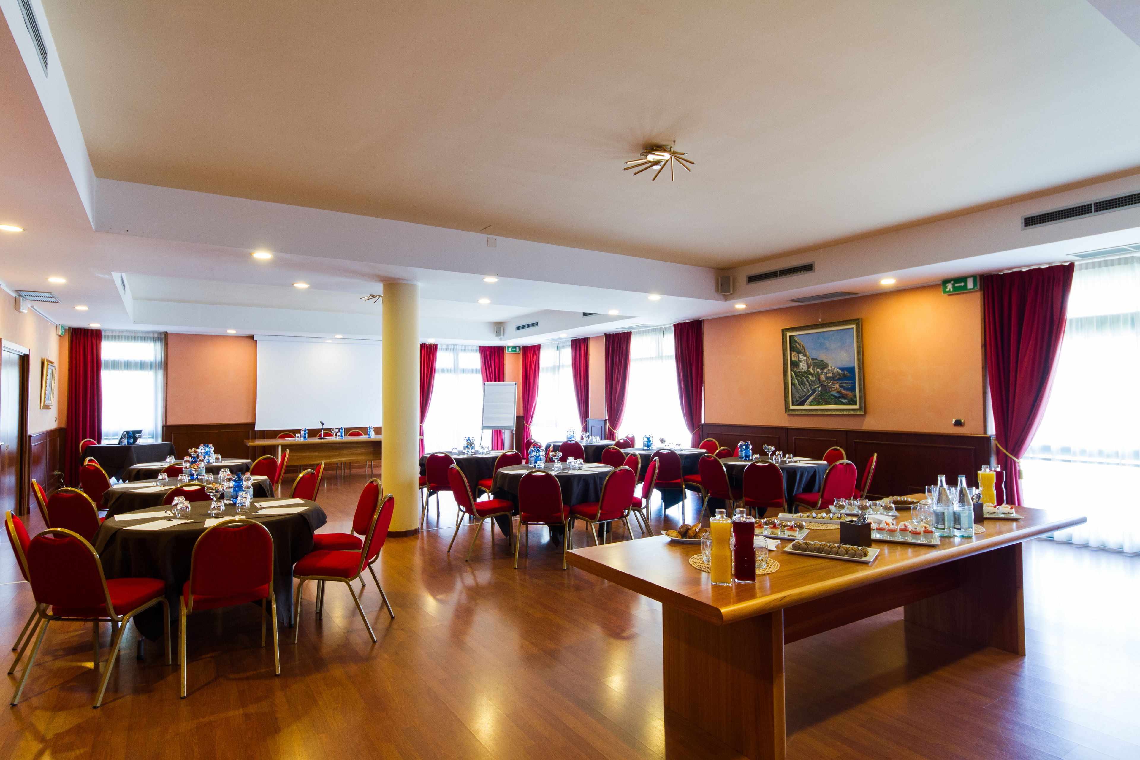 Une salle de conférence avec plusieurs tables, des chaises rouges et une longue table où sont disposés des plats et des boissons.