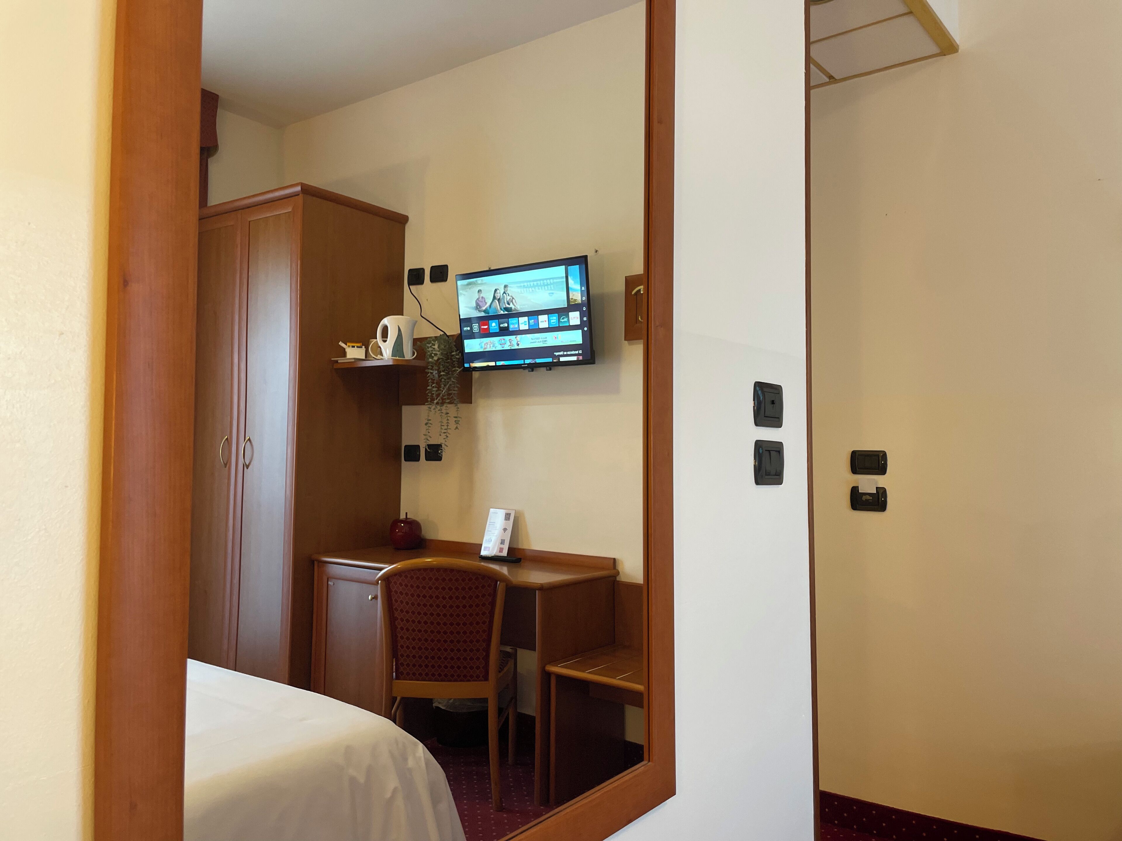A hotel room with a bed, a desk, a chair, a television mounted on the wall, and a wardrobe.