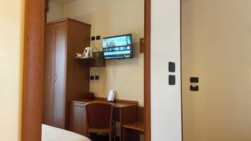 A hotel room with a bed, a desk, a chair, a television mounted on the wall, and a wardrobe.