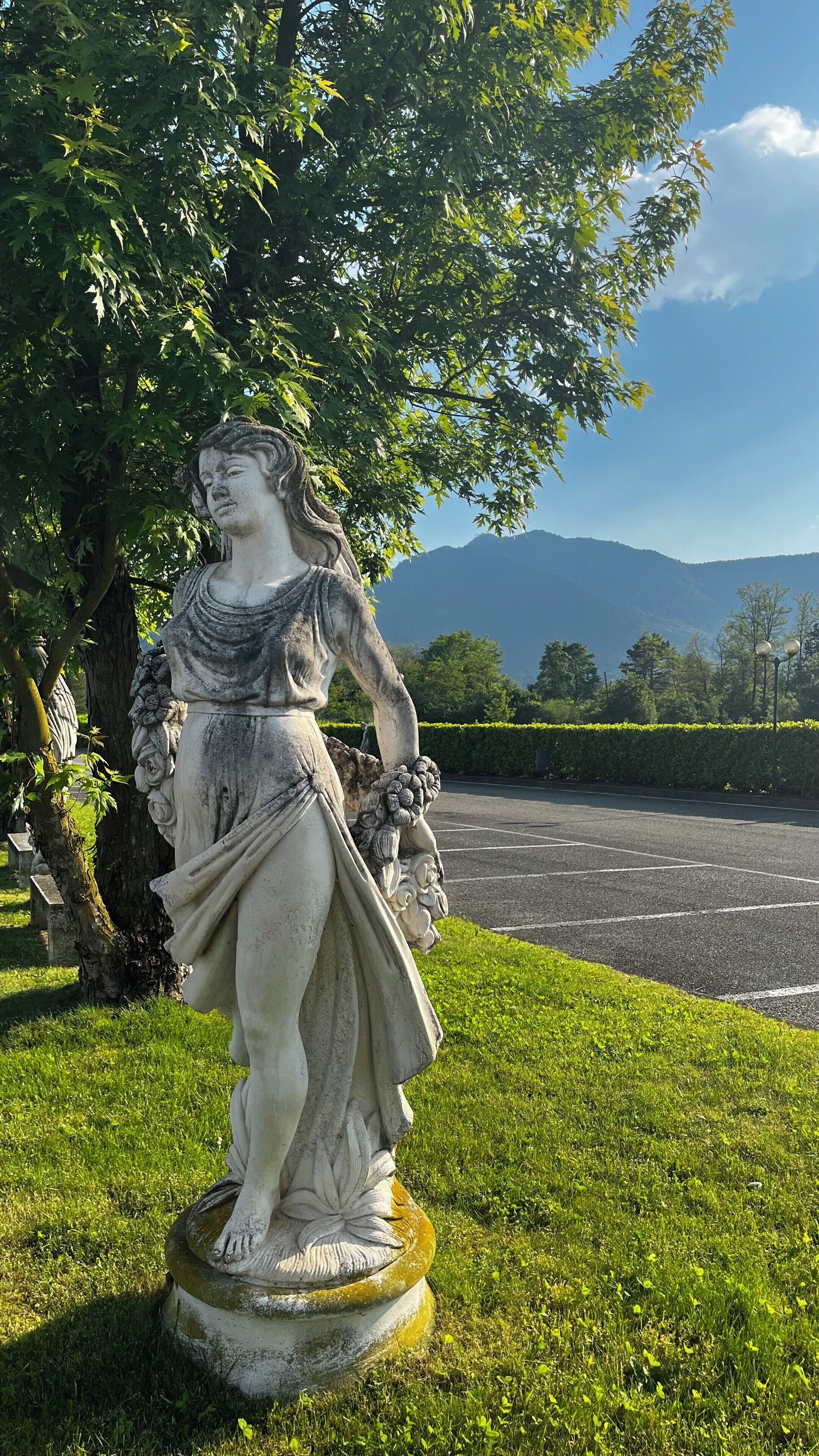 Une statue d’une femme dans un parc, avec un parking et des montagnes en arrière-plan.