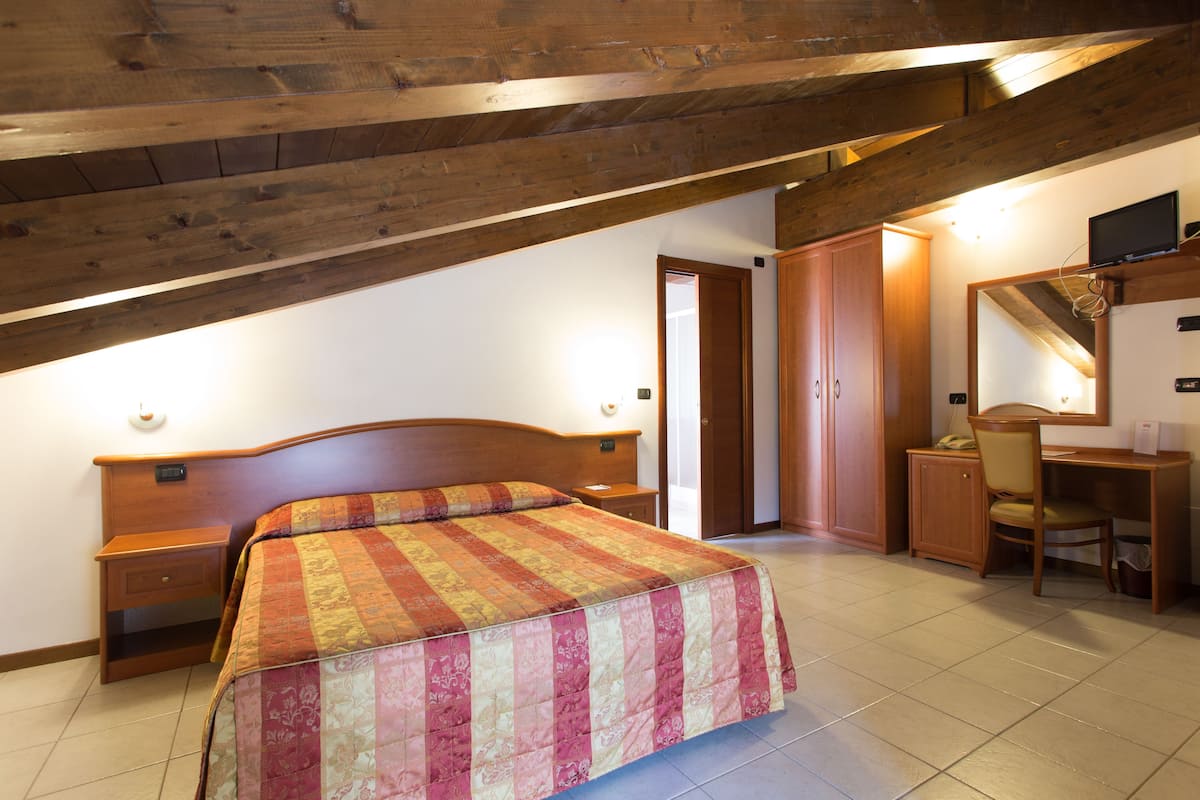 Ein Schlafzimmer mit Holzbalkendecke, einem Bett mit gemustertem Überwurf, einem Schreibtisch mit Stuhl und einem Kleiderschrank.