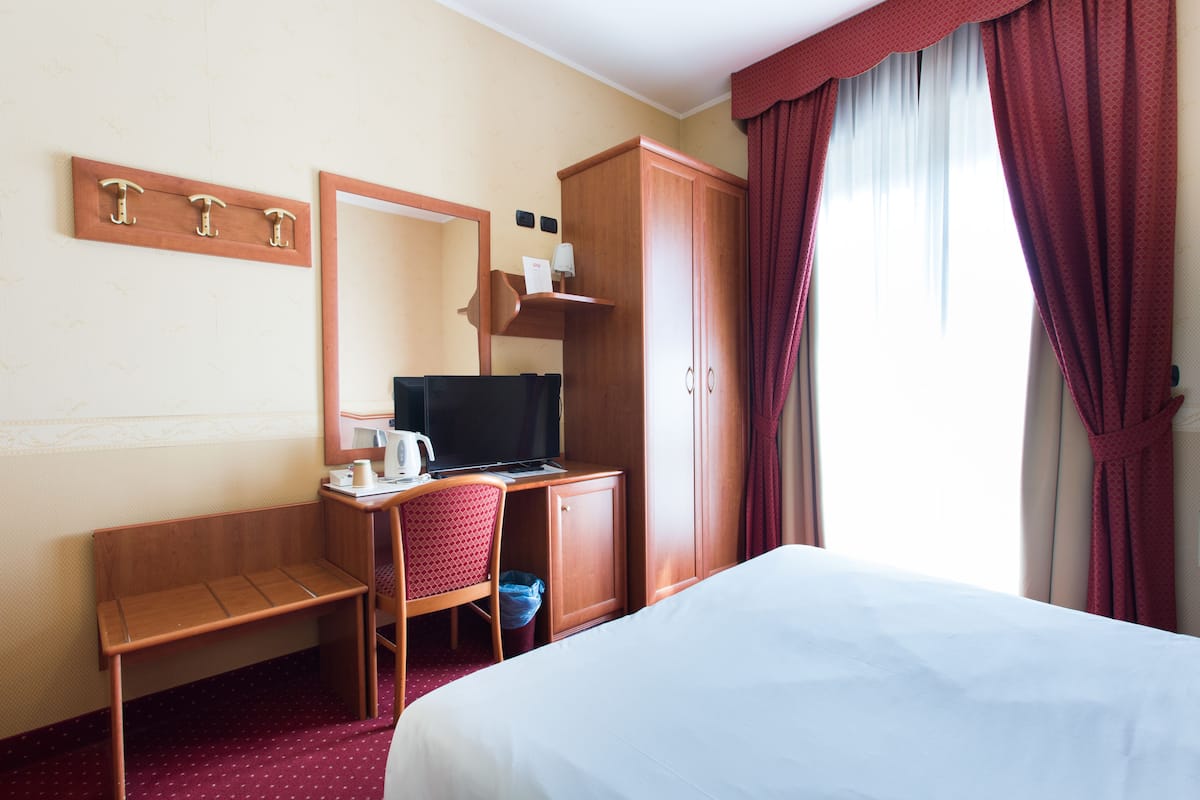Ein Hotelzimmer mit einem Bett, einem Schreibtisch mit Computer, einem Stuhl, einem Spiegel und einem Kleiderschrank.