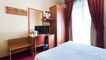 Una habitación de hotel con cama, escritorio con computadora, silla, espejo y armario.