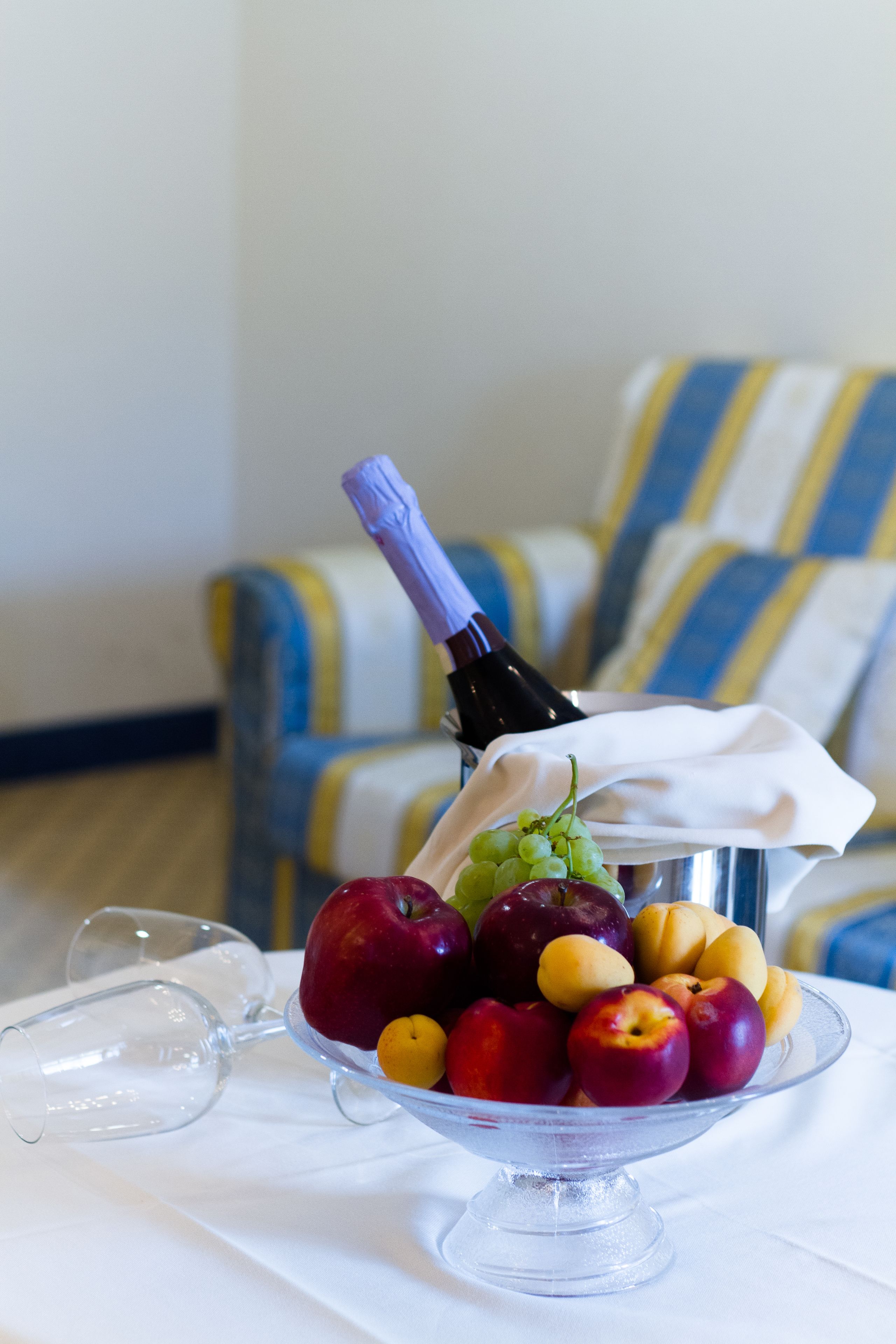 A fruit bowl with grapes, apples, and a bottle of wine on a table.