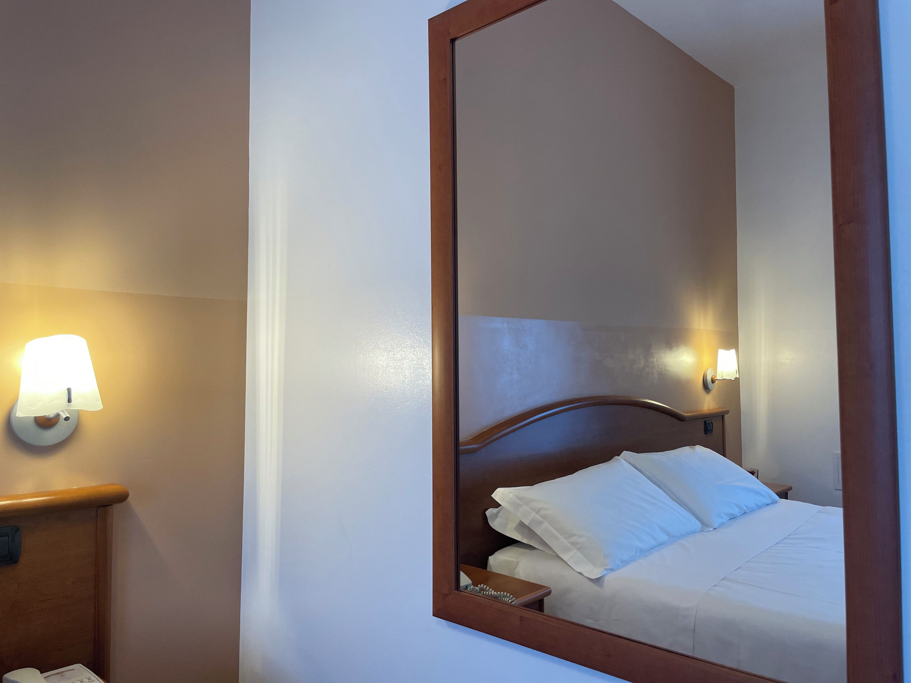 A hotel room with a bed, a nightstand, a lamp, and a mirror.