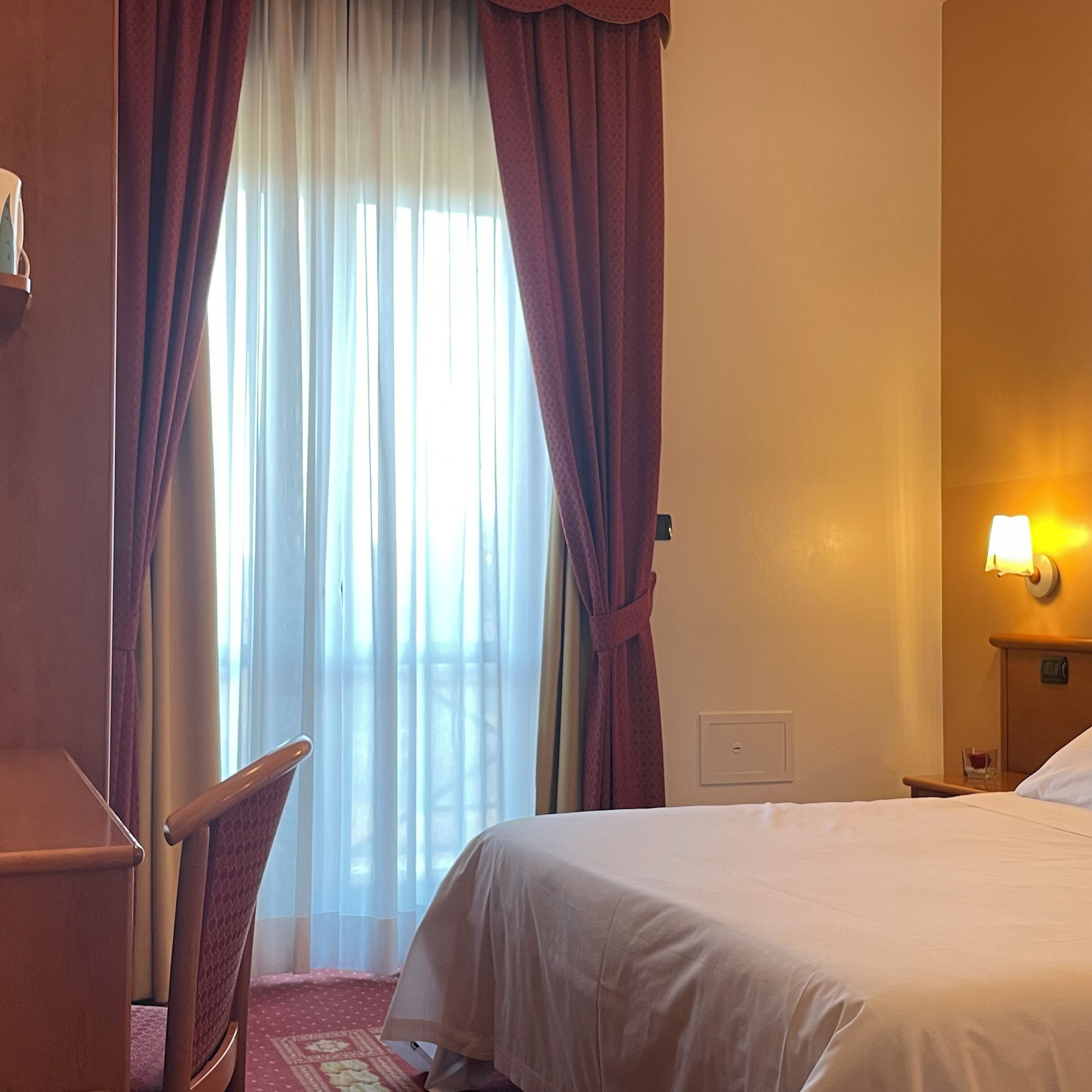 A hotel room with a bed, a chair, a nightstand, a lamp, and a window with curtains.