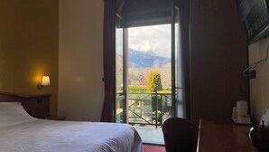 Habitación de hotel con cama, escritorio, silla, ventana con vista a las montañas y balcón.