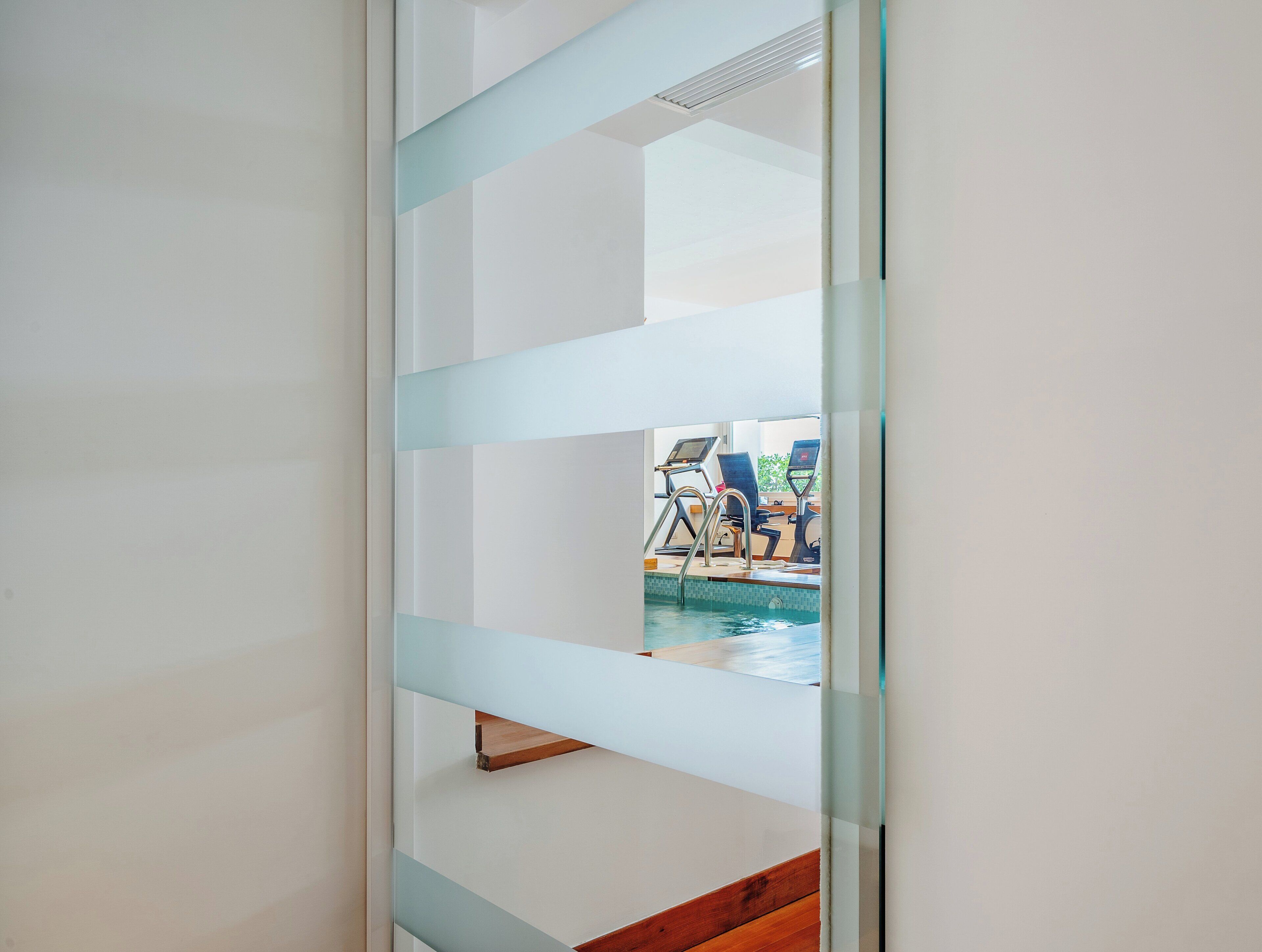 A view through a glass partition to a pool area with exercise equipment.