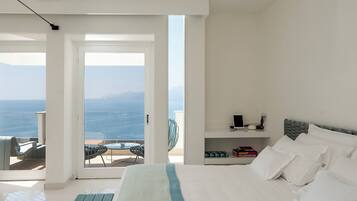 Un dormitorio con cama, mesita de noche, una silla y vista al mar.