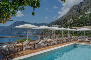A poolside area with lounge chairs and umbrellas, overlooking a mountainous coastline. - Casa Angelina (Praiano)