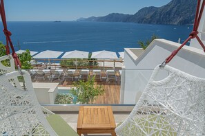 A balcony with white wicker furniture, a wooden table, and a pool. - Casa Angelina (Praiano)