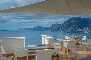 A terrace with tables and chairs overlooking a body of water and mountains. - Casa Angelina (Praiano)