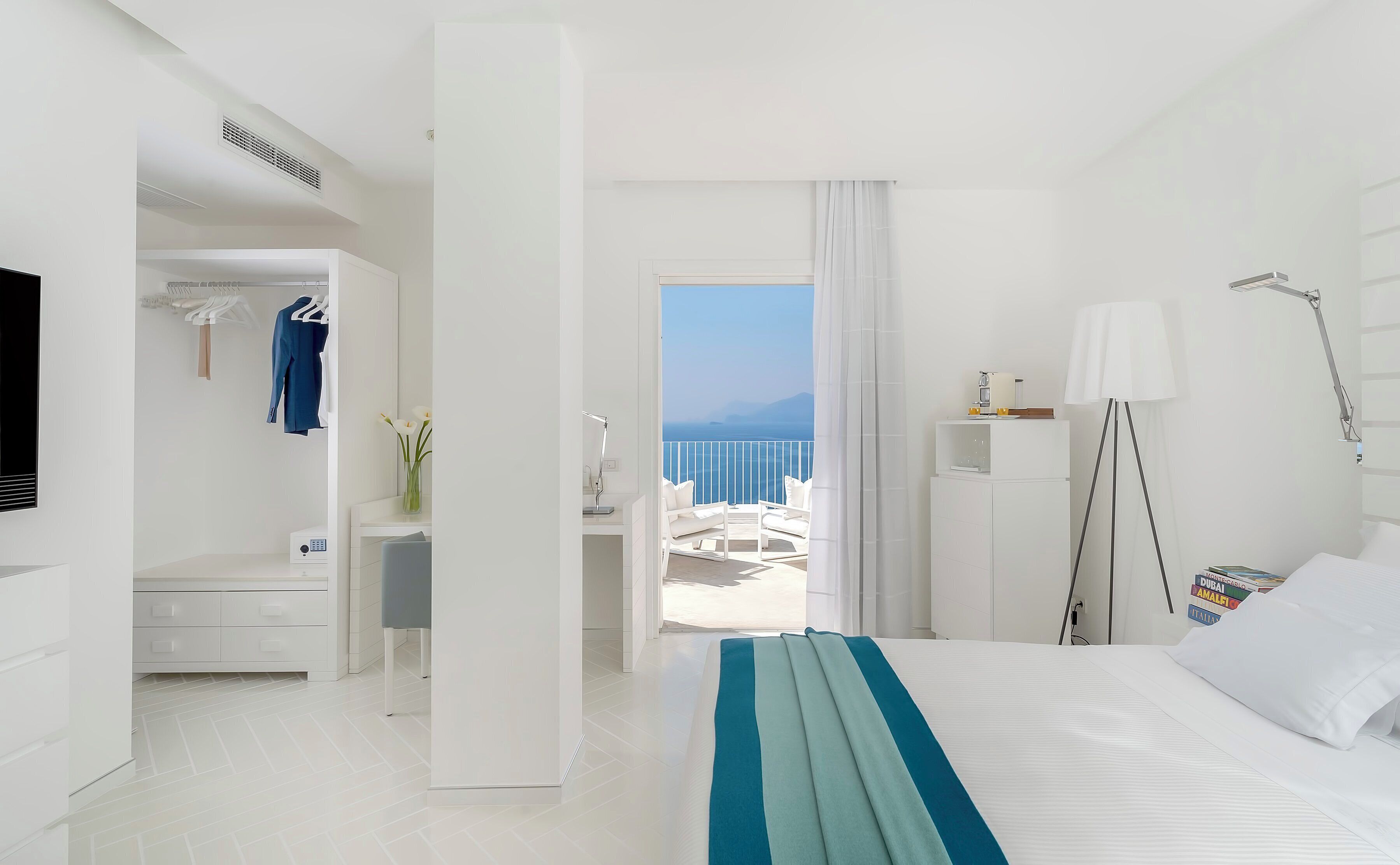 A modern hotel room with a bed, a desk, a chair, and a view of the sea.