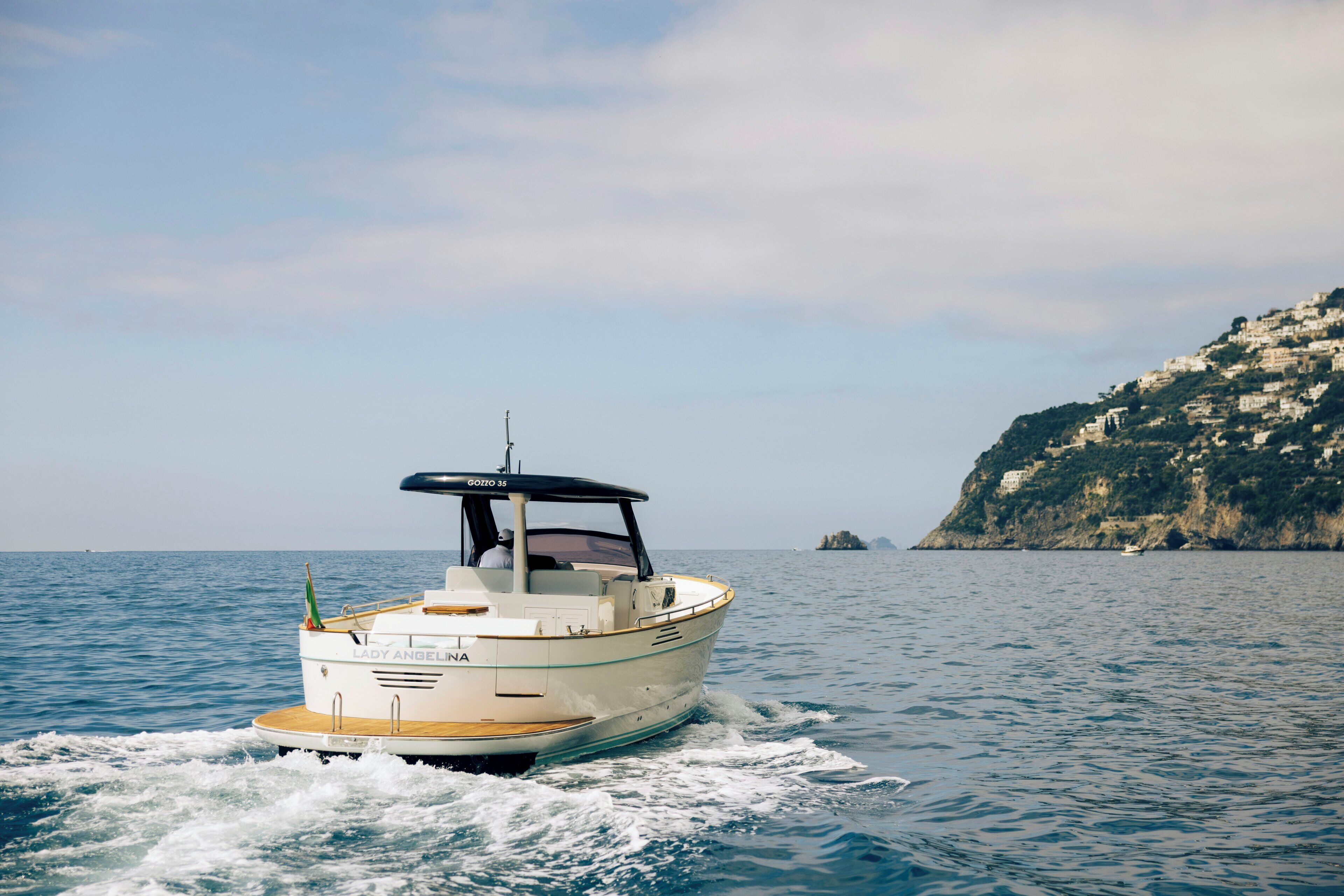 A boat named 'Lady Angelina' on a body of water with a coastal landscape in the background.