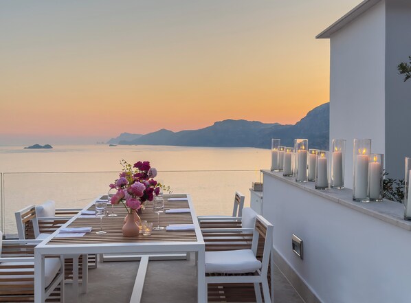 A terrace with a table set for dining, overlooking a calm sea and distant mountains. - Casa Angelina (Praiano)