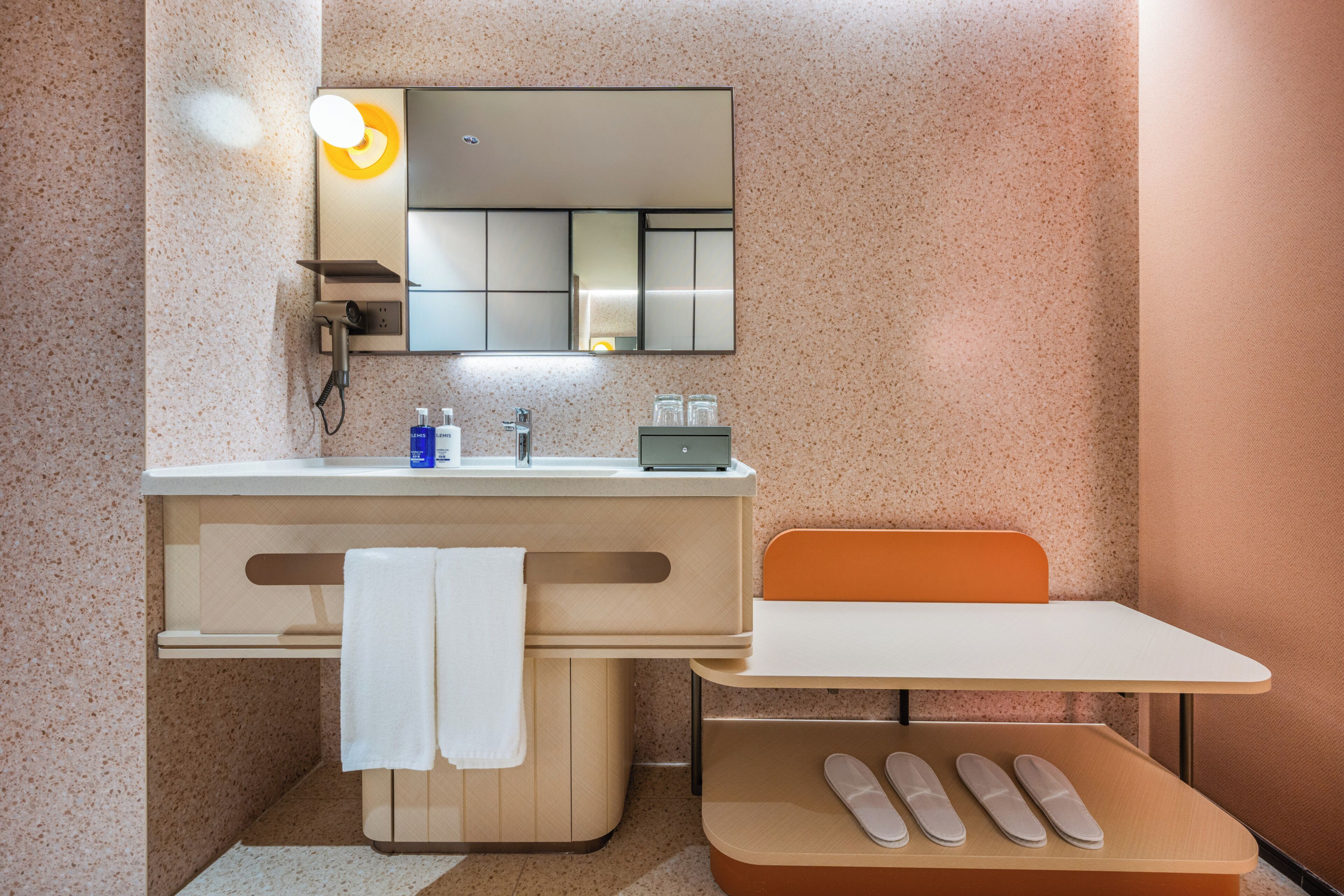 A bathroom with a sink, mirror, towel rack, and a table with slippers.