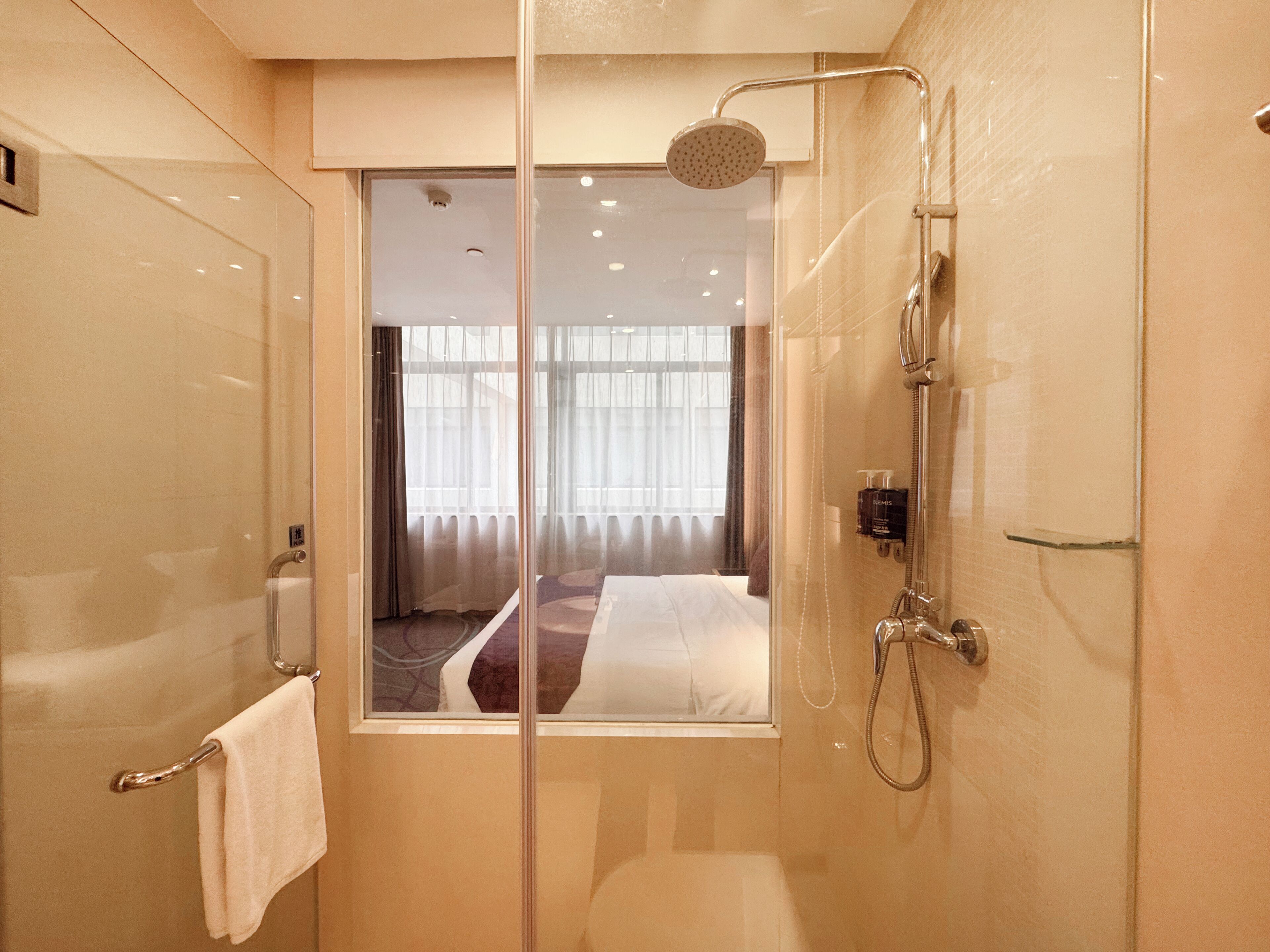 Un baño moderno con cabina de ducha de vidrio, una cama visible con cortinas y un perchero.
