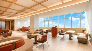 Un hall d’hôtel spacieux avec de hauts plafonds, de grandes fenêtres offrant une vue sur le ciel et divers types de sièges, notamment des canapés et des tables.