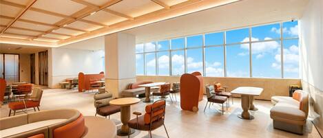 A spacious hotel lobby with high ceilings, large windows offering a view of the sky, and a variety of seating arrangements including sofas and tables.