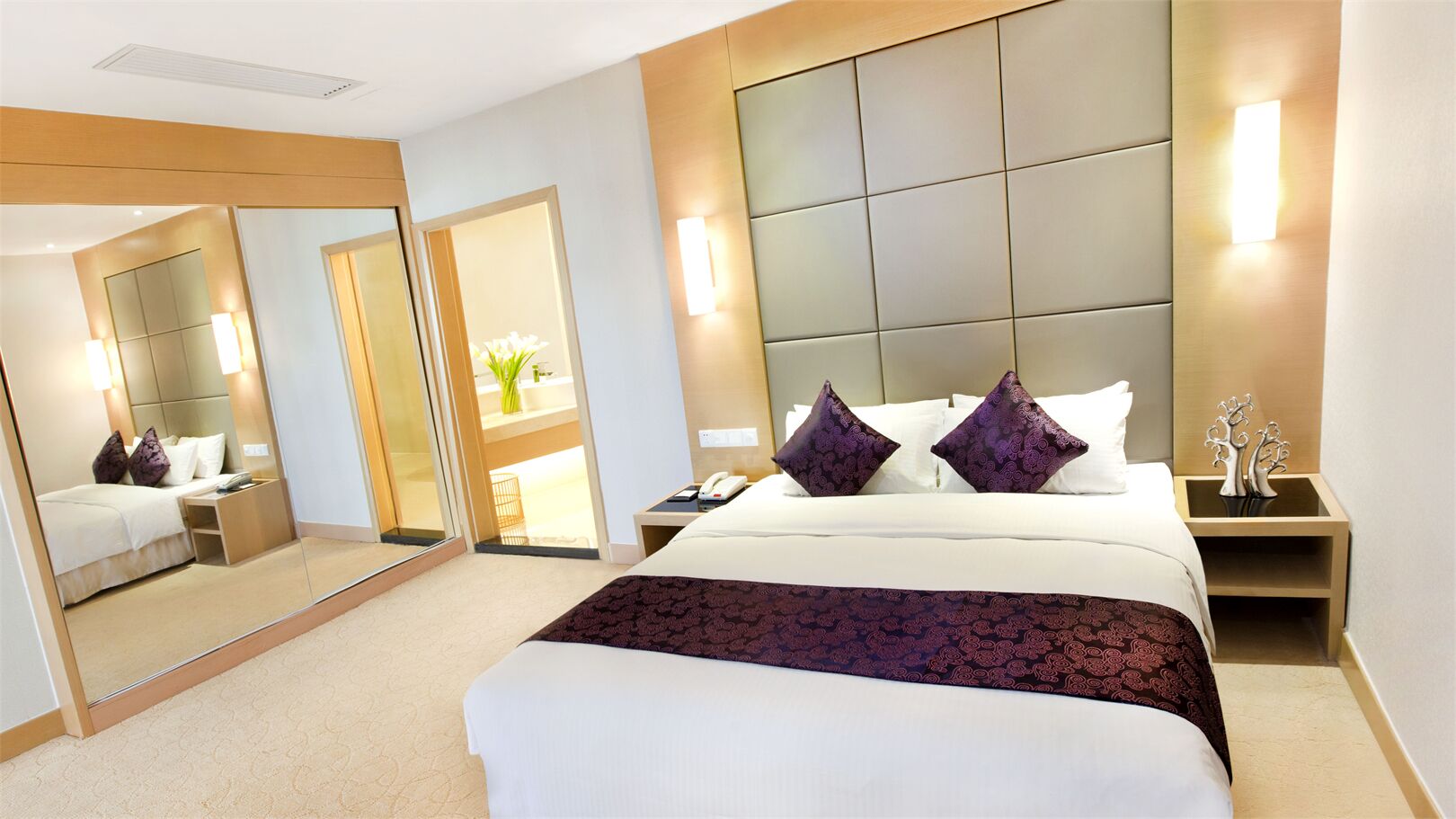 Quarto de hotel com cama grande, espelho, mesa de cabeceira e luminária na parede.