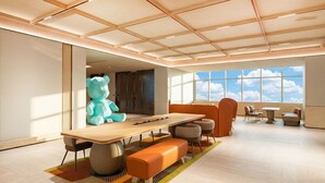 Un hall d’hôtel moderne avec une grande table, des sièges et une vue sur le ciel grâce à de larges fenêtres.