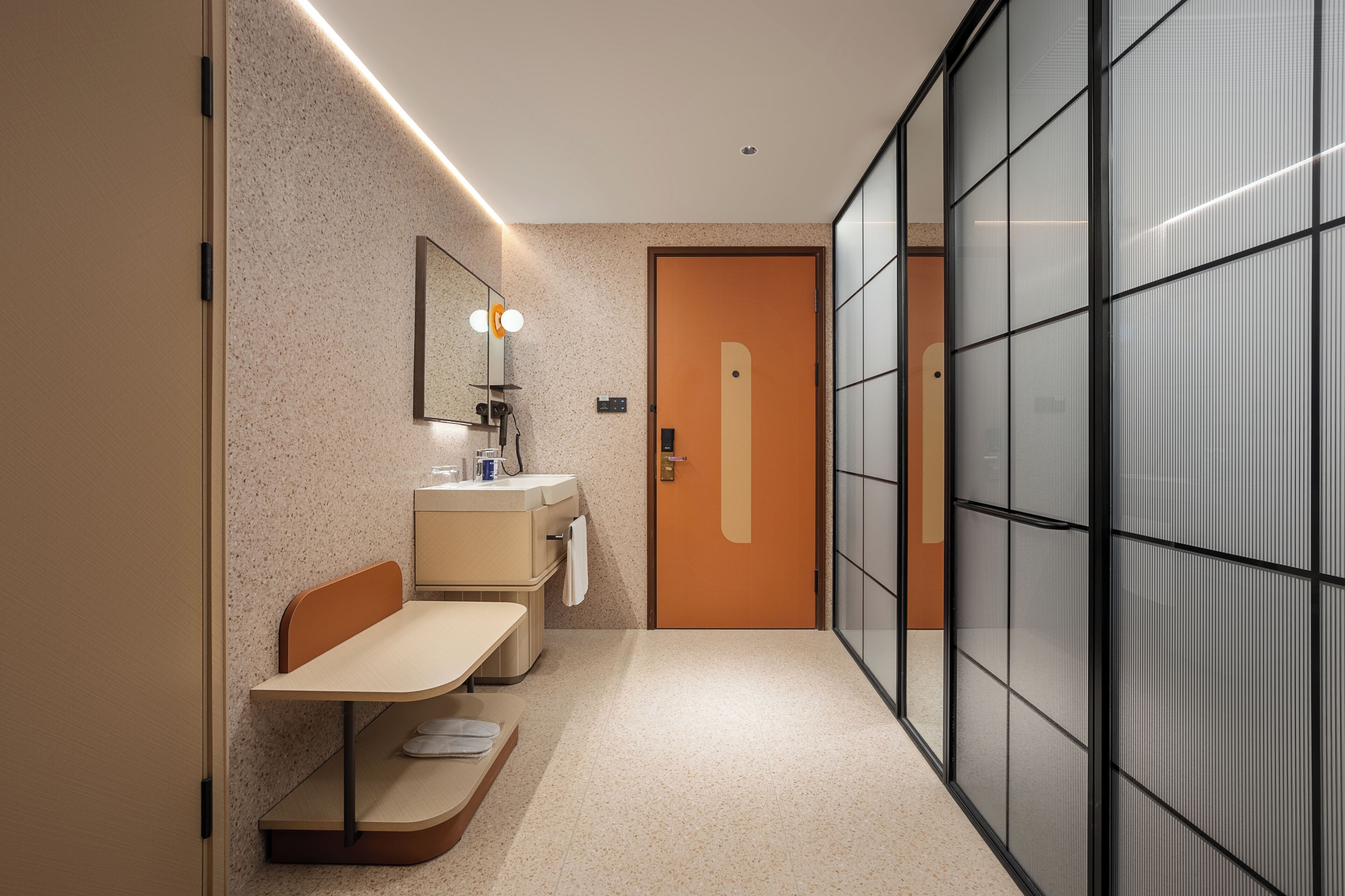 A narrow hallway with a small seating area, a mirror, and a door with a frosted glass panel.