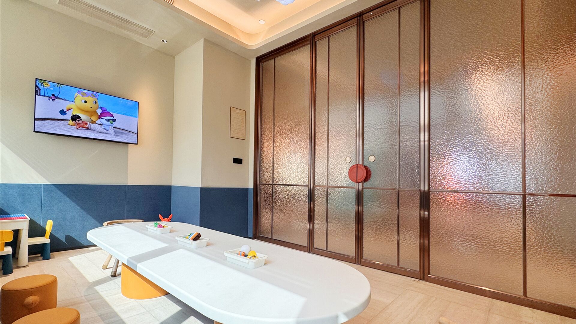 A modern room with a long white table, a TV on the wall, and a large sliding door with a textured glass panel.