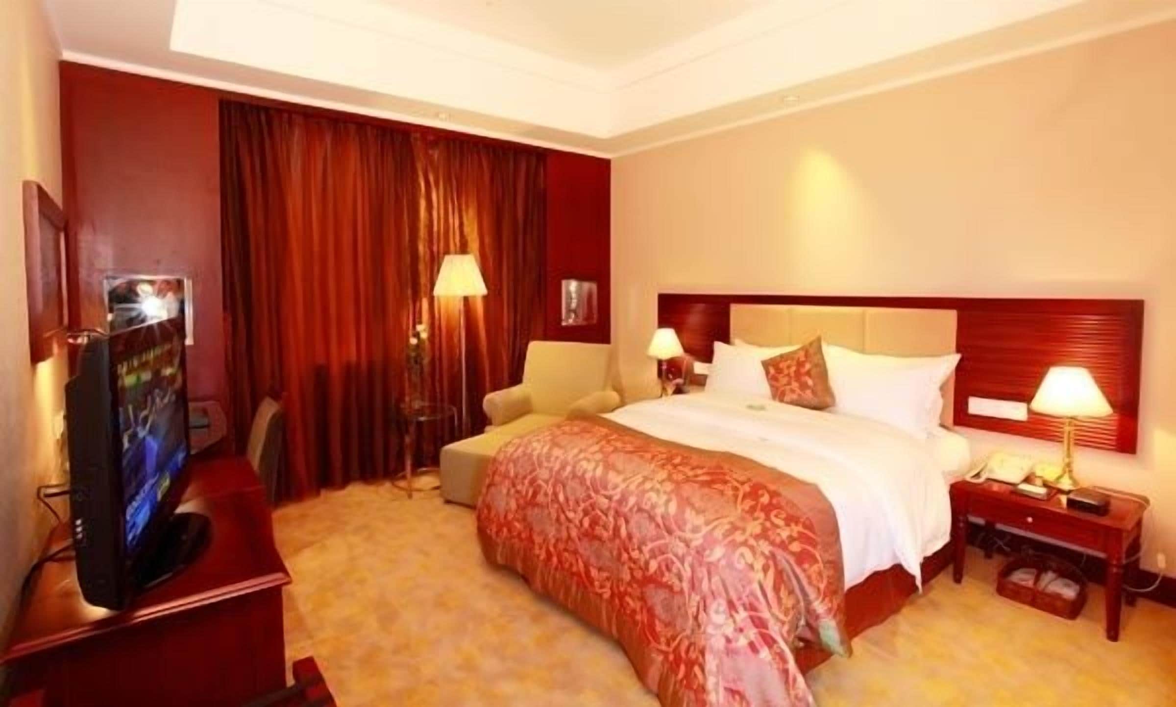 A hotel room with a large bed, a TV, a desk, and a chair.