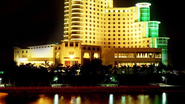 A large, multi-story hotel with a distinctive dome and cylindrical towers, featuring a reflective water body in front.