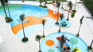 A large, multi-colored pool area with palm trees and a white deck surrounding it.