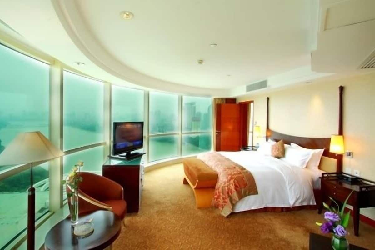 Een hotelkamer met een groot bed, een televisie, een bureau en uitzicht op de stad door grote ramen.
